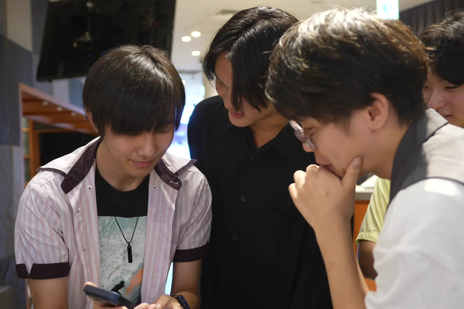 1台のスマートフォンを4人で囲んで覗き込む場面